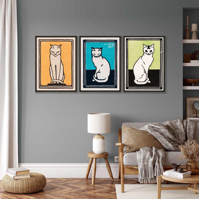 May include: Three framed prints of vintage cat illustrations. Each print features a white cat with black markings, sitting in a different colored background. The backgrounds are orange, blue, and green.
