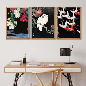K&ouml;nnte beinhalten: Drei gerahmte Drucke mit japanisch inspirierten Kunstwerken. Der linke Druck zeigt wei&szlig;e und rosa Blumen auf schwarzem Hintergrund mit einem blauen Fluss am unteren Rand. Der mittlere Druck zeigt einen wei&szlig;en Kakadu, der auf einem Ast mit roten Granatapfel Fr&uuml;chten sitzt. Der rechte Druck zeigt eine Schar roter und wei&szlig;er Kraniche, die vor einem schwarzen Hintergrund fliegen.