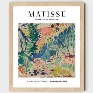 May include: A framed print of a painting by Henri Matisse titled "Landscape at Collioure". The painting features a colorful landscape with green trees, blue sky, and pink flowers. The print is framed in a light wood frame.