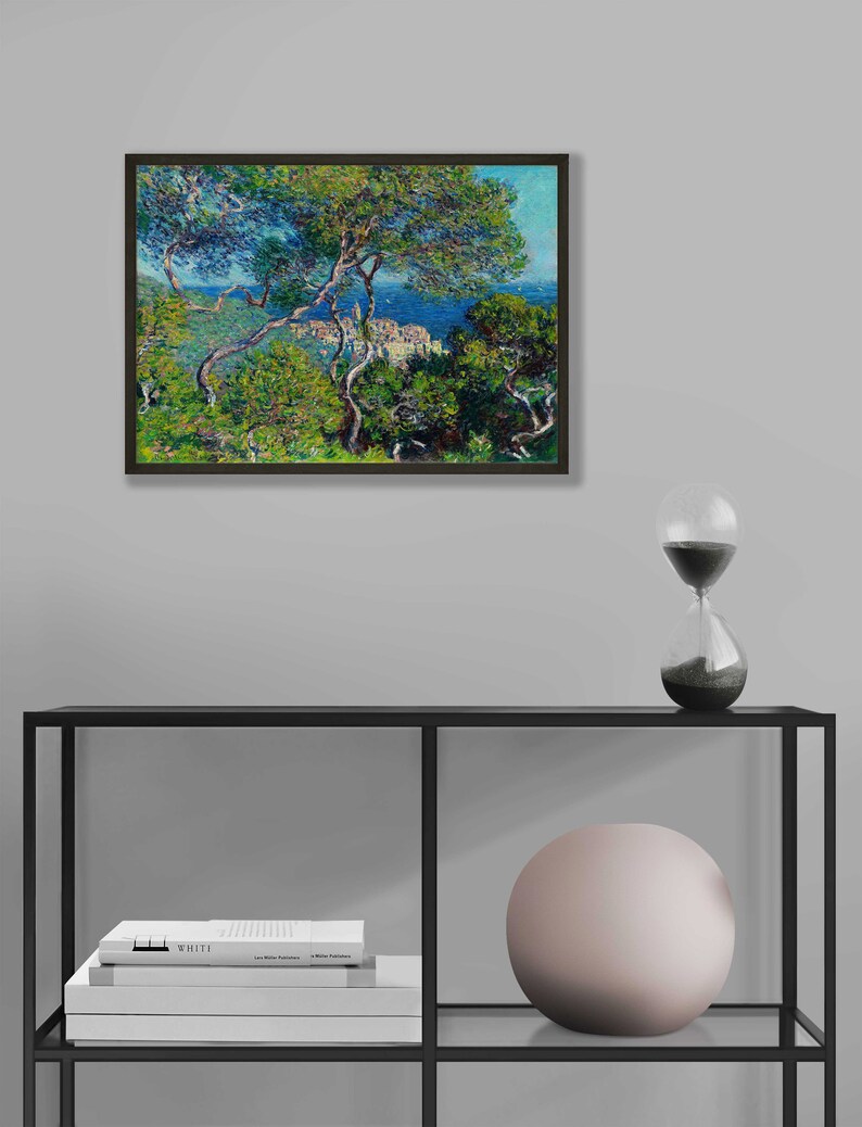 May include: A framed painting of a landscape with a view of a town on a hill overlooking the ocean. The painting is done in a style reminiscent of Impressionism, with visible brushstrokes and a focus on light and color. The painting is framed in a dark wood frame.