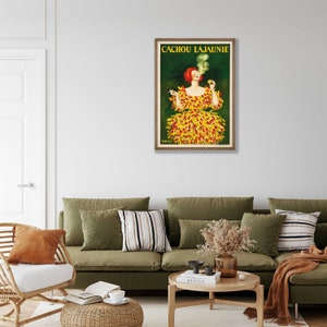 May include: Vintage poster advertising Cachou Lajaunie, a French brand of breath mints. The poster features a woman in a yellow and red dress, smoking a cigarette and holding a box of Cachou Lajaunie.