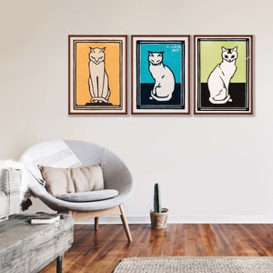 May include: Three framed prints of white cats in different poses. The cats are on a yellow, blue, and green background. The frames are brown wood.