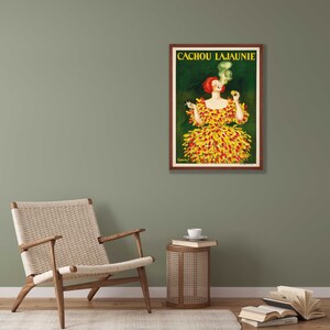 May include: A vintage poster advertising Cachou Lajaunie, a brand of cough drops. The poster features a woman in a yellow and red dress, smoking a cigarette and holding a box of Cachou Lajaunie.
