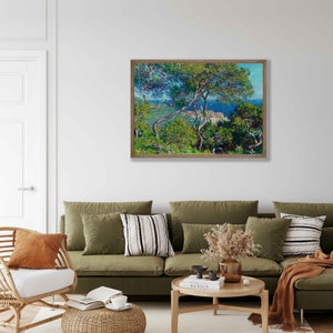 May include: A framed painting of a landscape scene with a view of a town from a hilltop. The painting features a bright blue sky, green trees, and a small town in the distance. The painting is framed in a simple wooden frame.