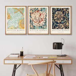 May include: Three framed prints of floral patterns by William Morris. The prints are in a modern home office setting with a wooden desk, chair, and lamp.