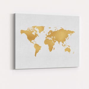 Op de afbeelding: Vierkante canvas print met een goudkleurige wereldkaart op een witte achtergrond. De continenten zijn in goud weergegeven, wat contrasteert met het wit. Het kunstwerk is gemonteerd op een wit canvas.