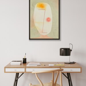 May include: A framed abstract wall art print featuring a pale, oval-shaped head against a muted sage green background. The artwork includes a bright yellow patch at the top, a soft red circle on the right, and a thin, dark red geometric line.