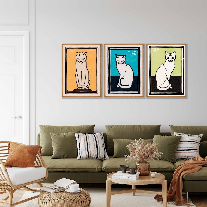 May include: Three framed prints of stylized black and white cat illustrations. The cats are sitting and facing forward. The frames are wood with a light brown finish. The background is a white wall.