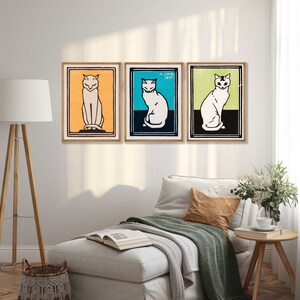 May include: Three framed prints of stylized black and white illustrations of cats. The cats are sitting and facing forward. The frames are wood with a light brown finish. The background is a white wall.