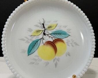 May include: White, round plate with a beaded edge. The plate features a colorful illustration of two yellow and brown peaches with green and blue leaves. The plate is supported by gold-colored stands.