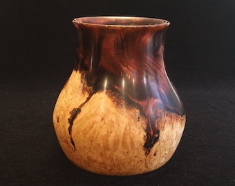 May include: A wooden vase with a unique, marbled pattern in shades of brown, black, and purple. The vase has a rounded, bulbous shape and a smooth, polished finish.