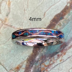 A 4mm wide stainless steel ring rests on a green and brown stone background.  The ring has blue opal inlayed with a strand of copper winding in a sine wave pattern through the channel.