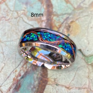 An 8mm wide stainless steel ring rests on a green and brown stone background.  The ring has blue opal inlayed with a strand of copper winding in a sine wave pattern through the channel.