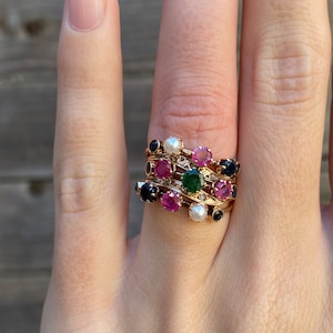 May include: A gold ring with multiple bands featuring a variety of gemstones, including rubies, sapphires, emeralds, and pearls.