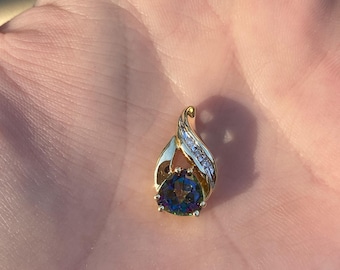 May include: A gold pendant with a blue and green gemstone surrounded by smaller clear gemstones.