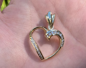May include: A gold heart-shaped pendant with a row of small clear stones around the edge.