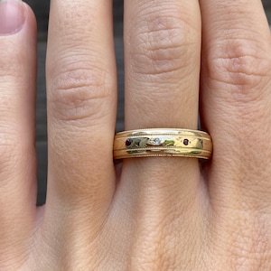 May include: A gold band ring with two small red gemstones and a single white gemstone.