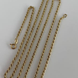 Puede incluir: Varias cadenas de cuerda doradas de diferentes longitudes se muestran sobre un fondo blanco. Las cadenas tienen un dise&ntilde;o de cuerda trenzada y est&aacute;n conectadas con un cierre. Las cadenas probablemente est&aacute;n hechas de oro o metal dorado.