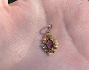 May include: A gold pendant with a purple gemstone surrounded by small white pearls. The pendant is in the shape of a flower with a pointed center.