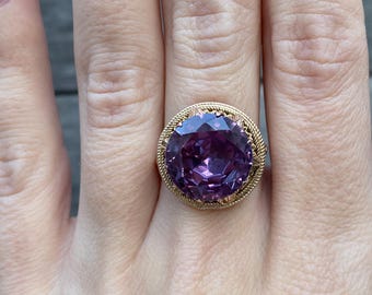 May include: A gold ring with a large, round, purple gemstone set in a delicate, filigree design.