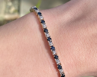 May include: A gold tennis bracelet with alternating black and white round stones.