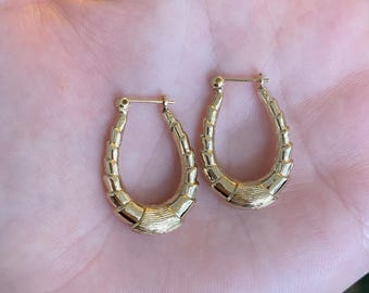 May include: A pair of gold-colored hoop earrings. Each earring has a textured, segmented design with a rounded, oval shape. The earrings are displayed against a neutral background.
