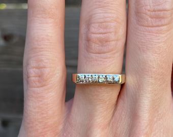 May include: A gold band ring with a row of small, clear diamonds.