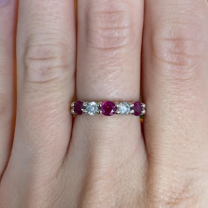 May include: A gold ring with a band set with alternating rubies and diamonds. The ring has five gemstones: three rubies and two diamonds. The gemstones are set in a row across the top of the ring.
