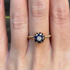 May include: A gold ring with a blue enamel flower design and a small diamond in the center.