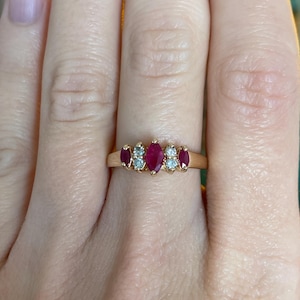 May include: A gold ring with a series of gemstones. The ring has three oval-cut, deep red rubies and four smaller, round, clear gemstones. The ring is set on a gold band.
