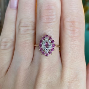 May include: A gold ring featuring a cluster of pink gemstones and small white diamonds. The ring's design is oval-shaped, with the gemstones arranged around a central diamond cluster. The ring is set on a thin gold band.