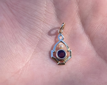 May include: A gold pendant with a purple gemstone and a small pearl. The pendant is in the shape of a teardrop with a geometric design.