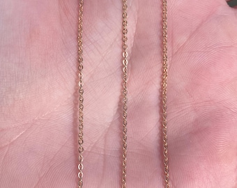 May include: A rose gold chain necklace with a delicate, thin chain link design. The chain is shown laid out on a hand, demonstrating its length and flexibility.
