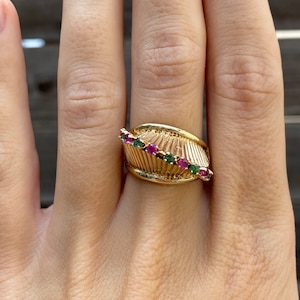 May include: A gold ring with a textured band and a row of pink and green gemstones.