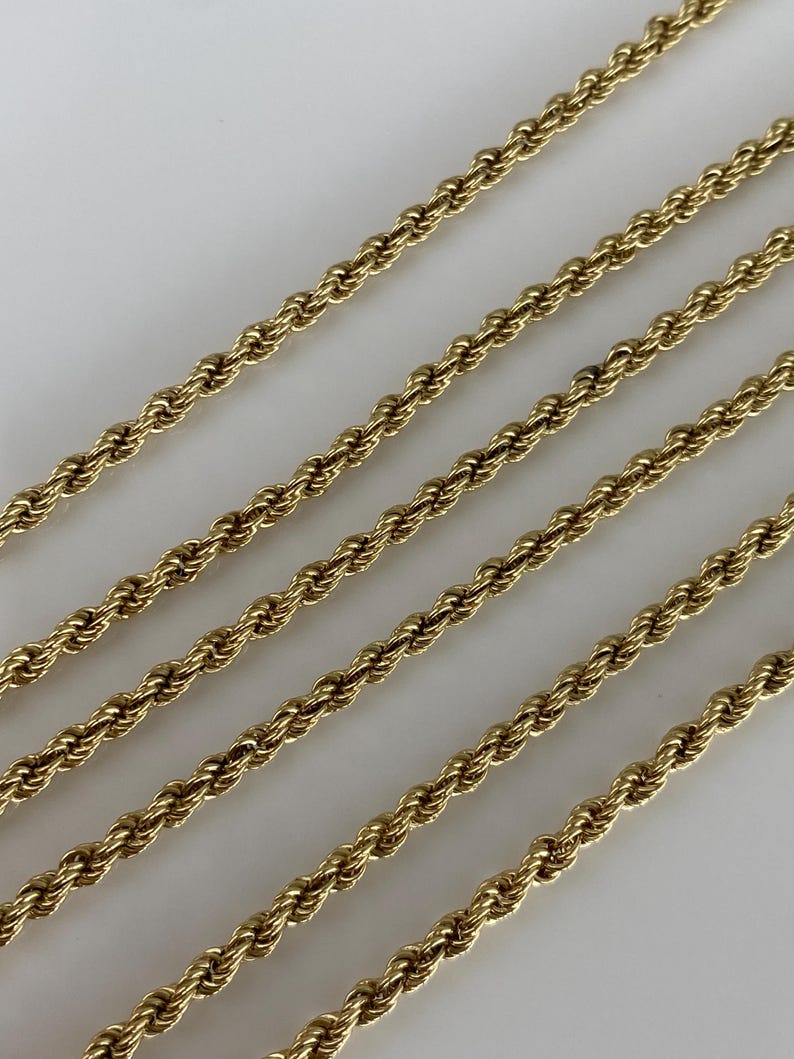 Puede incluir: Primer plano de varias cadenas de cuerda de color dorado. Las cadenas est&aacute;n dispuestas en diagonal sobre un fondo blanco. Las cadenas tienen un dise&ntilde;o de cuerda trenzada, y el color dorado es brillante y reluciente. Las cadenas son probablemente joyas.