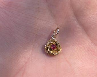 May include: A gold pendant with a red gemstone in the center, shaped like a rose.