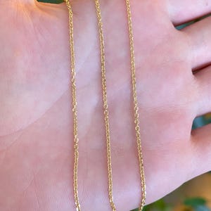 May include: A delicate gold chain necklace featuring a series of small, uniform, interlocking circular links. The metal has a bright, reflective finish that catches the light, creating a consistent, polished appearance along the entire length of the chain.