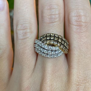 May include: A two-tone ring with a woven design. The top section is dark brown, the lower section is bright white. The ring is set with small stones, creating a textured surface. The ring is worn on a finger.