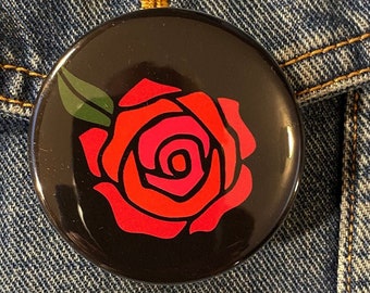 May include: A black button featuring a red rose design. The rose is stylised and has a pink centre.