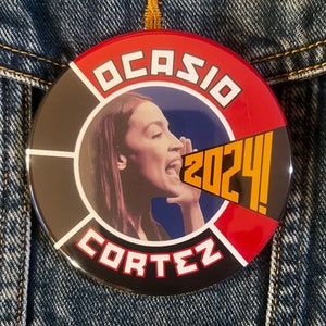 May include: A red, white, and black button with a picture of a woman speaking into a megaphone. The text "OCASIO CORTEZ 2024!" is printed on the button.