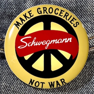 May include: A yellow button with a peace sign and the text "Make Groceries Not War" and "Schwegmann" in red.