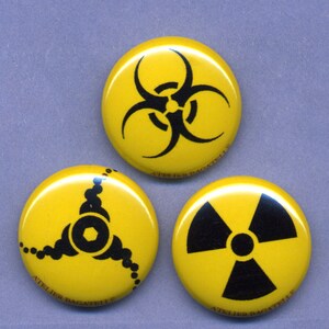 May include: Three yellow round buttons with black symbols. The first button has a biohazard symbol, the second button has a stylized triangle with a circle in the center, and the third button has a radiation symbol. All buttons have the text "Atelier Bagatelle" printed on the bottom.