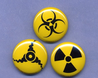 May include: Three yellow round buttons with black symbols. The first button has a biohazard symbol, the second button has a stylized triangle with a circle in the center, and the third button has a radiation symbol. All buttons have the text "Atelier Bagatelle" printed on the bottom.