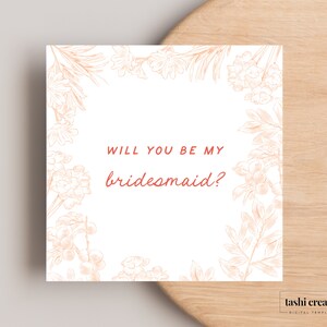 May include: Square invitation card with floral illustrations in peach tones. The text "WILL YOU BE MY bridesmaid?" is written in a coral color. The card is on a wooden surface.
