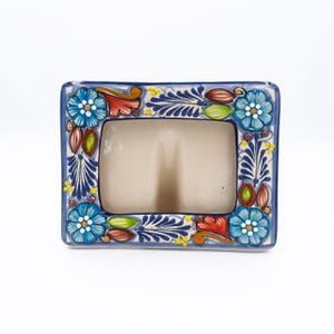 May include: A rectangular ceramic soap dish with a blue border and floral design. The dish features a central compartment and is decorated with blue flowers, red accents, and green leaves. The soap dish is approximately 6 inches long and 4 inches wide.