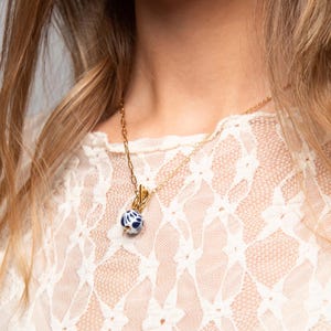 May include: A gold chain necklace with a blue and white ceramic pendant. The pendant is round and has a floral design.