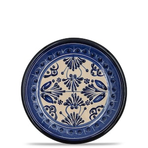 May include: Round ceramic plate with a blue and cream floral design. The plate has a dark blue rim and a central cream-colored area with a repeating pattern of blue stylized flowers and leaves. The plate is likely for decorative or serving purposes.