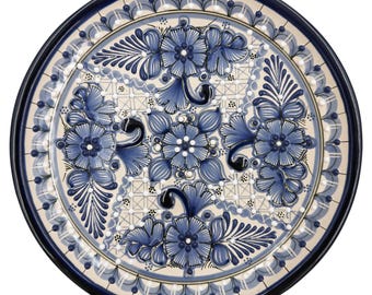 May include: Circular ceramic plate with a hand-painted floral pattern. The plate has a cream-coloured centre adorned with blue flowers and foliage. The rim is dark blue, and the design is symmetrical and detailed, suitable for serving or display.