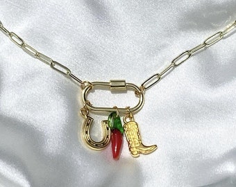 May include: A gold chain necklace with a gold carabiner clasp and three charms: a horseshoe, a red chili pepper, and a gold cowboy boot.