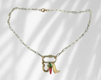 May include: A gold chain necklace with a gold carabiner clasp and three charms: a horseshoe, a red chili pepper, and a gold cowboy boot.